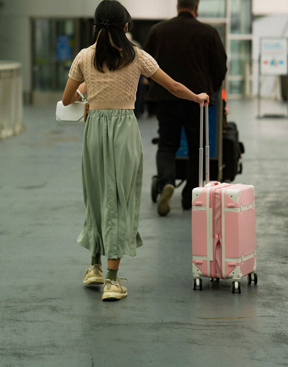 Viajante caminhando com a mala rosa pelo saguão do aeroporto